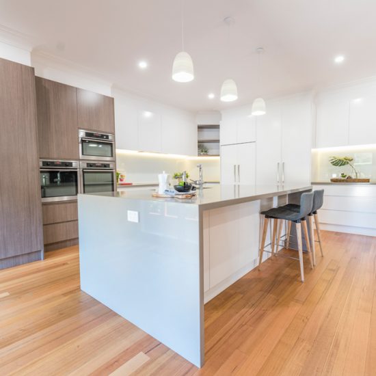 Kitchen design, contemporary kitchen, woodgrain laminate, stone benchtops, waterfall edge, lighting over island, white kitchen, glass splashback, white splashback, integrated fridge, push close doors, handle-free